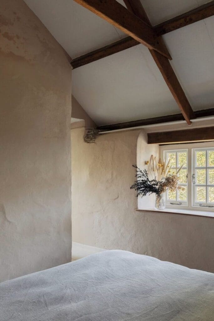 Rustic bedroom with limewash or plaster walls and explosed beam ceiling