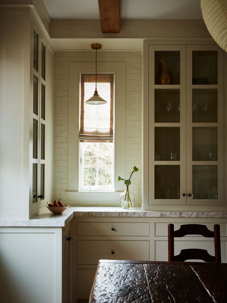 Classic pared back kitchen with glass cabinetry, bamboo blind, and marble countertops